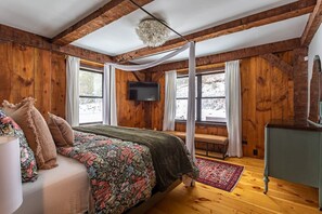 Een slaapkamer met houten lambrisering, een bed, een bankje, een televisie en een groot raam.
