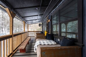 Une cabane dotée d’une terrasse en bois, d’un banc et d’un lit recouvert d’une couverture à carreaux.