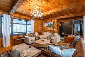 A cozy living room with a wooden ceiling, a large window, a fireplace, and a comfortable seating area.
