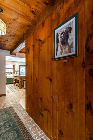 A wooden hallway with a framed picture of a dog, a kitchen area with a green countertop, and a patterned rug.