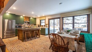 A kitchen with a central island, green cabinets, and a large window with a snowy view. - Lux Hot Tub Cabin w Fire Pit (Napanoch)