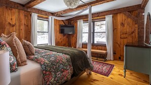 A wooden-paneled bedroom with a bed, a bench, a television, and a large window. - Lux Hot Tub Cabin w Fire Pit (Napanoch)