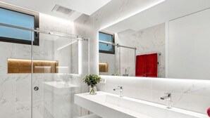 Un baño moderno con un espejo grande, azulejos de mármol blanco y un mueble de tocador blanco.
