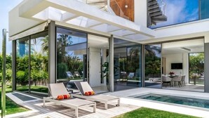 Una casa moderna con piscina, puertas de cristal y mobiliario de exterior.