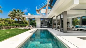 Ein modernes Haus mit Swimmingpool, Sitzgelegenheiten im Freien und einer Treppe zu einer oberen Ebene.