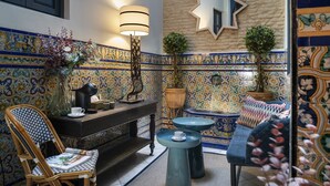 Une pièce avec un mur recouvert de carreaux, une console en bois, une chaise, une lampe et deux petites tables rondes.