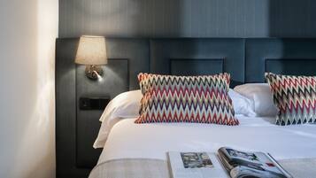Een hotelkamer met een bed, kussens, een lamp en een tijdschrift.