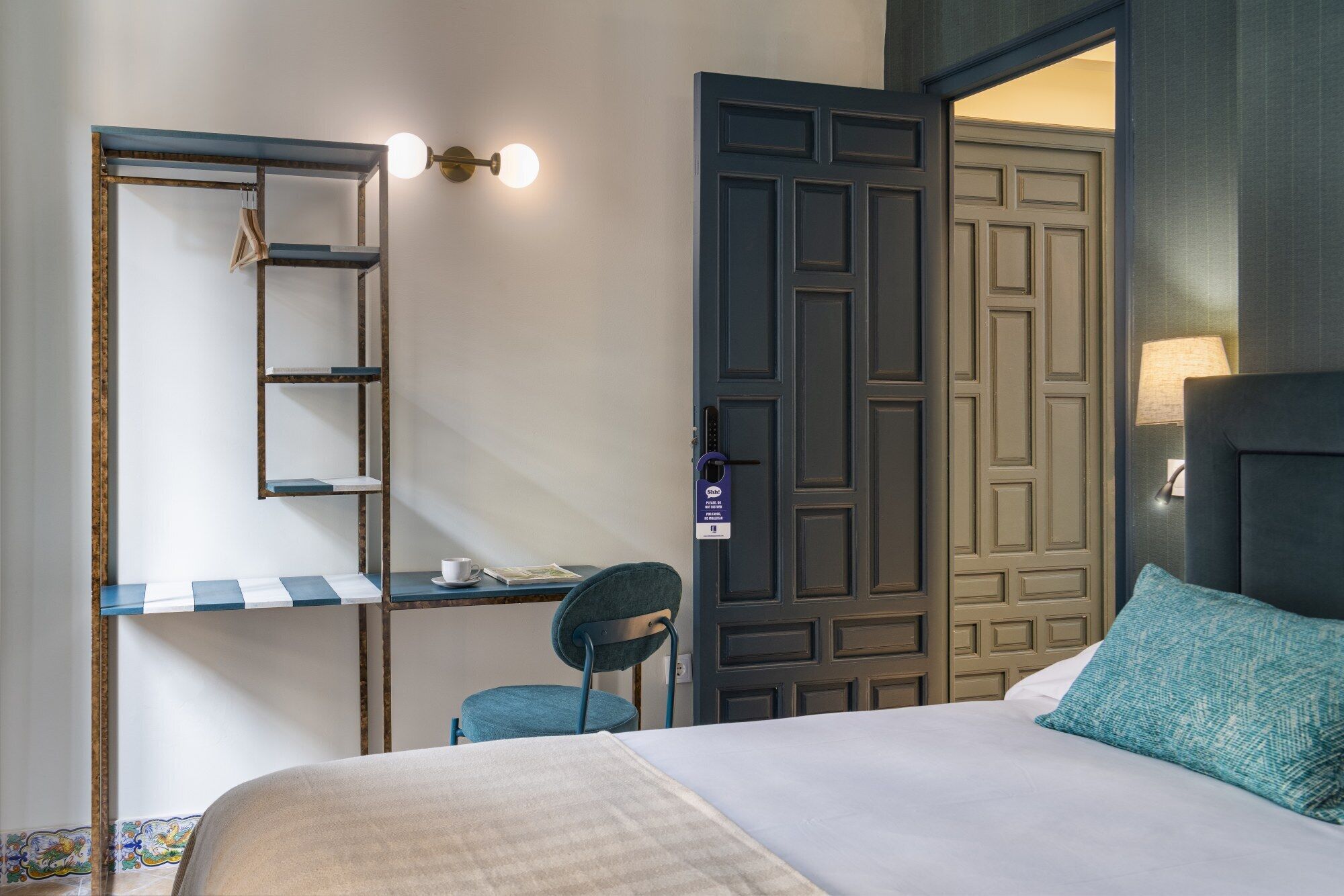 A hotel room with a bed, a desk with a chair, a wardrobe, and a door.