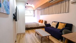 A compact room with a bed, a sofa, a small table, and a TV. - J-Court Oshiage (Tokyo)