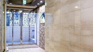 A corridor with a marble wall, a glass door with a metal frame, and a patterned wall on the left. - J-Court Oshiage (Tokyo)