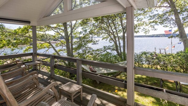 A wooden deck with benches overlooking a body of water, a hammock, and an American flag.