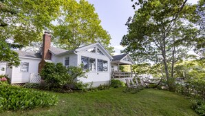 A white house with a porch, a brick chimney, and a grassy yard with a small tree and a swing set.