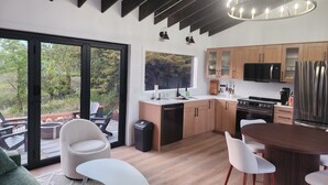 A modern kitchen with wooden cabinets, a stainless steel refrigerator, and a large window overlooking a deck.