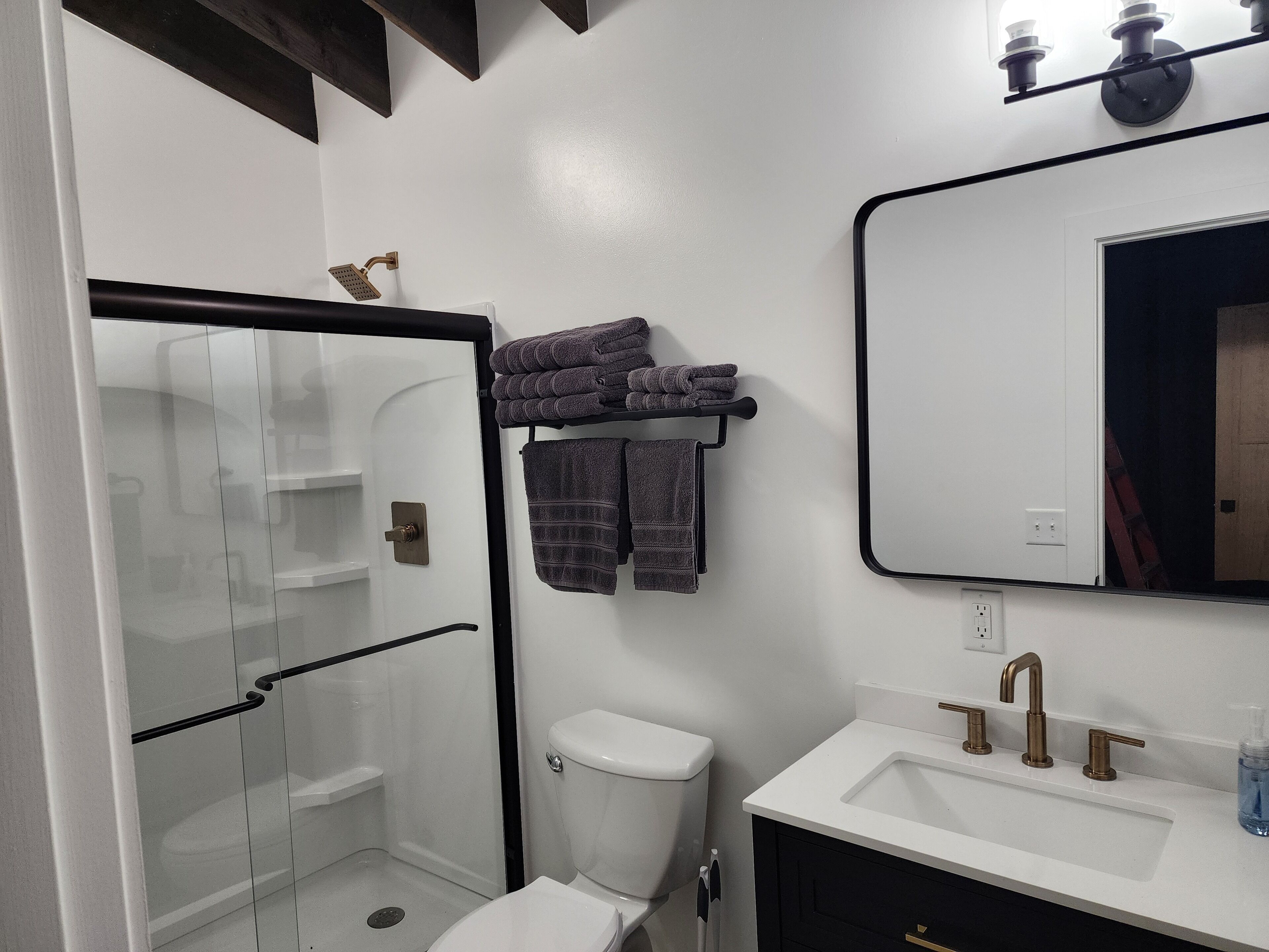 Un baño moderno con cabina de ducha de vidrio, inodoro, lavabo con espejo y toallero con toallas dobladas.