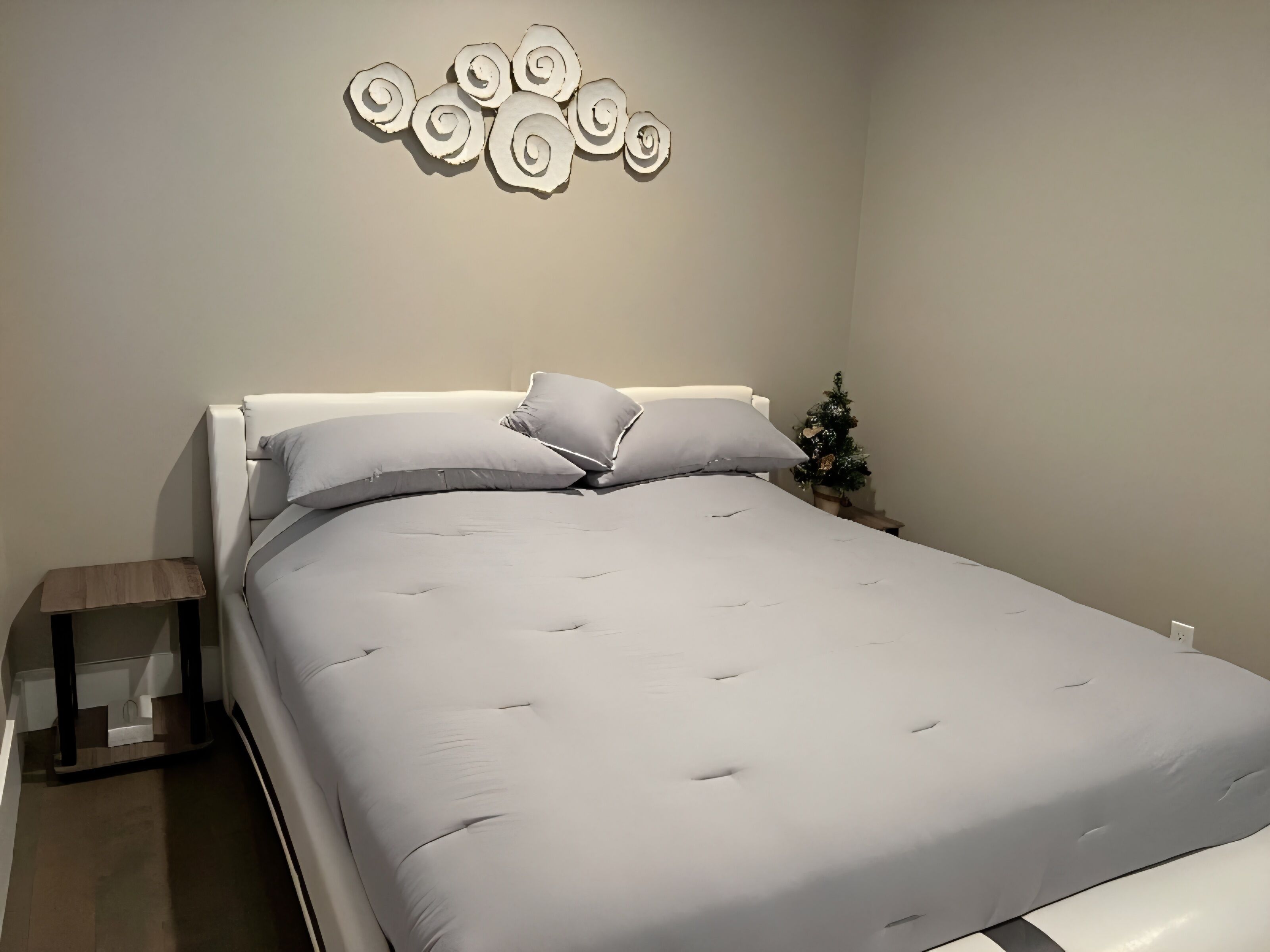 Un lit bien fait, avec une tête de lit blanche, une petite table de chevet avec une lampe, et un élément décoratif fixé au mur au-dessus du lit.