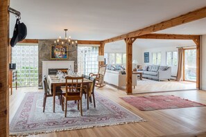 Een ruime woonkamer met een open haard, een eettafel met stoelen en een bank.