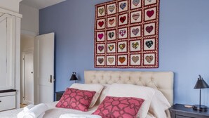 Une chambre à coucher avec un lit, des oreillers, un tableau décoratif au mur et une table de chevet.