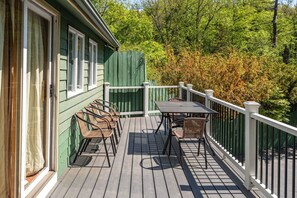 A wooden deck with a table and chairs, surrounded by a white railing, and a green fence in the background.
