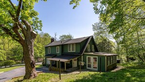 Une maison verte avec un porche couvert, une cheminée et une cour clôturée.