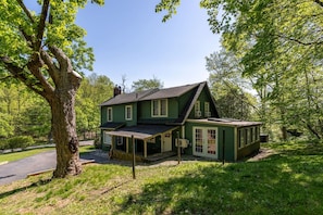 A green house with a covered porch, a chimney, and a fenced yard.