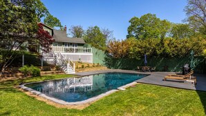 Un jardin avec une piscine, une terrasse en bois et un espace clôturé, avec une maison en arrière-plan.