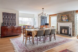 A dining area with a wooden table set for four, a chandelier, and a fireplace with a stone wall.
