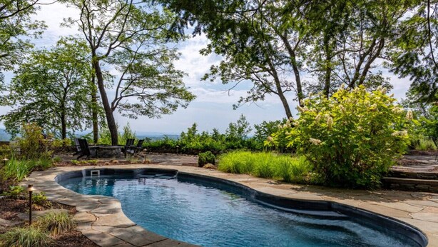 Une piscine à bordures incurvées, entourée de carreaux de pierre et d’une végétation luxuriante.