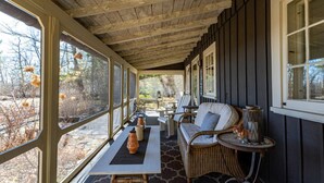 Une véranda avec un canapé et une table en osier, de grandes fenêtres et une vue sur les arbres.