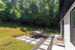 Un patio con tavolo e sedie, circondato da un vialetto in pietra e un'area verde alberata.