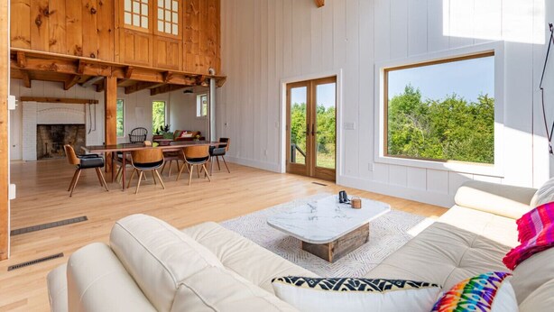 Un vaste espace de vie doté d’un plafond en bois, d’une table à manger avec des chaises, d’un canapé et d’une grande fenêtre donnant sur un paysage verdoyant.