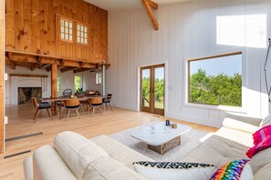 Un vaste espace de vie doté d’un plafond en bois, d’une table à manger avec des chaises, d’un canapé et d’une grande fenêtre donnant sur un paysage verdoyant.
