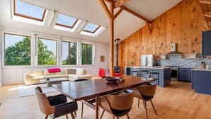Une cuisine moderne aux murs en bois, un coin repas avec une table et des chaises en bois, et de grandes fenêtres offrant une vue sur les arbres.