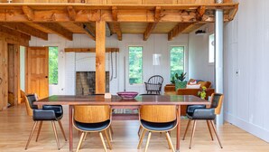 Une table à manger en bois, avec quatre chaises, une cheminée et une vue sur la verdure à l’extérieur.