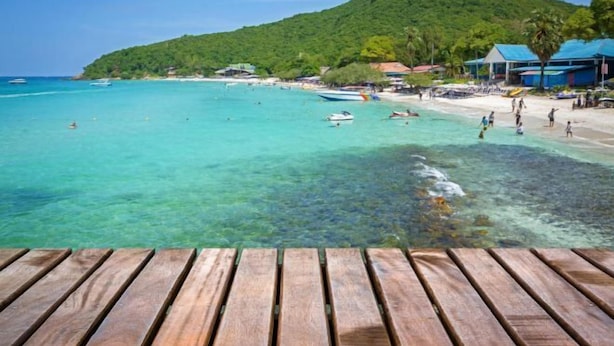 A wooden deck overlooking a beach with clear turquoise water, boats, and a mountainous backdrop. - Le Soleil Koh Larn (Koh Larn)