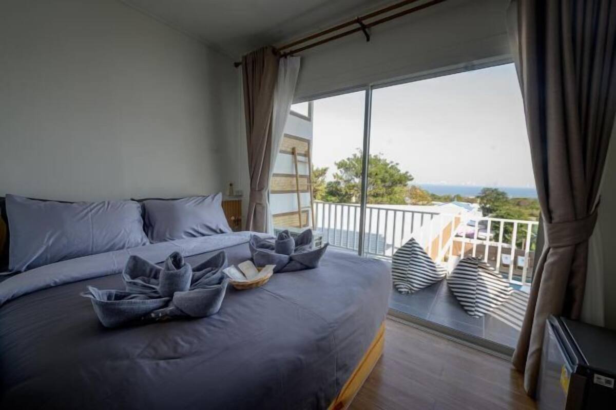 A bedroom with a large bed, a small balcony with a view, and a window with curtains.