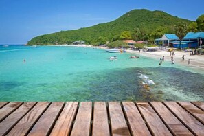 A wooden deck overlooking a beach with clear turquoise water, a mountain in the background, and beach umbrellas. - Le Soleil Koh Larn (Koh Larn)