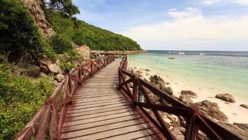 A wooden boardwalk leading to a beach with clear water and a rocky shoreline.