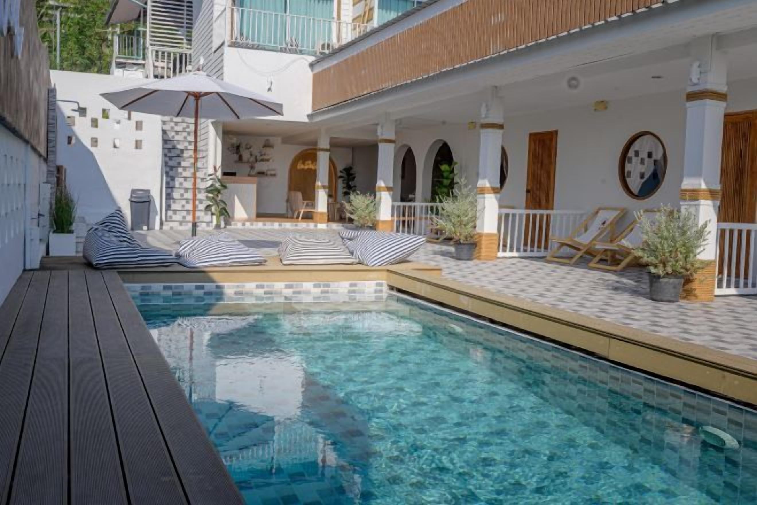 A swimming pool with a wooden deck, lounge chairs, and a covered area with a table and chairs.