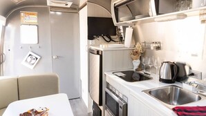 A compact kitchenette with a sink, stove, microwave, and a small refrigerator. - Desert Dream Airstream with Pool (Yucca Valley)