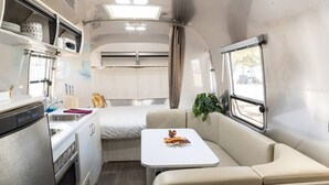 A compact RV interior with a kitchenette, a dining area, and a sleeping berth. - Desert Dream Airstream with Pool (Yucca Valley)