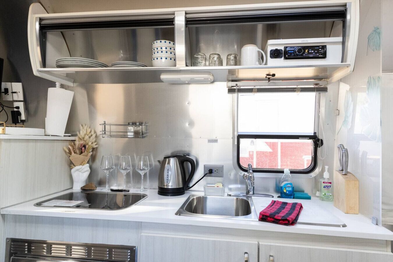 A compact kitchenette with a stainless steel sink, a kettle, and a small window.