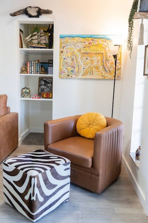 Un salon avec un fauteuil en cuir marron, un pouf à motifs zébrés, une bibliothèque et une carte colorée accrochée au mur.