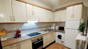 Une cuisine compacte équipée d’un évier, d’une cuisinière, d’un four à micro-ondes et d’un lave-linge.