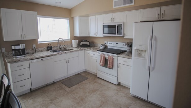 Una cocina con gabinetes blancos, microondas, refrigerador, estufa y lavaplatos.