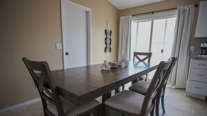 Un comedor con una mesa de madera y cuatro sillas, un jarrón decorativo y un armario blanco al fondo.