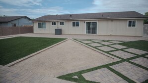 Una casa de un piso con patio trasero cercado, terraza pavimentada y césped.