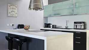 Une cuisine moderne dotée d’un îlot central, de tabourets de bar noirs, d’une machine à café et d’un grille-pain.