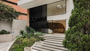 A modern building with a staircase leading to a glass door, surrounded by greenery and a brick wall. - Lomm By Somos The Group (Medellín)