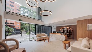 A modern hotel lobby with a reception desk, seating area, and large windows overlooking the street. - Lomm By Somos The Group (Medellín)