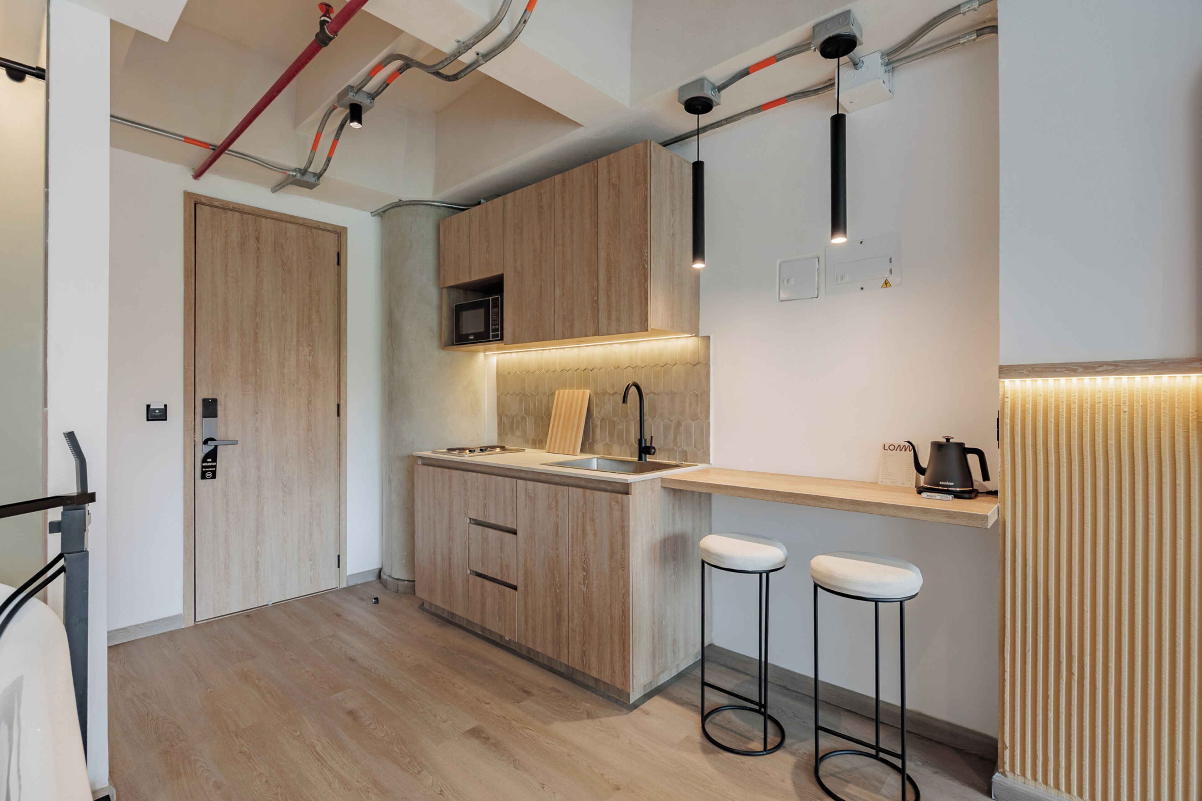 A modern kitchen with wooden cabinets, a microwave, a sink, and two bar stools.